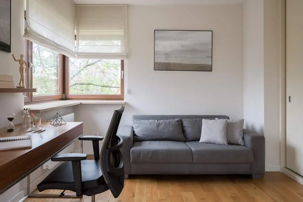 Stylish home office room with window, grey sofa and wooden floor