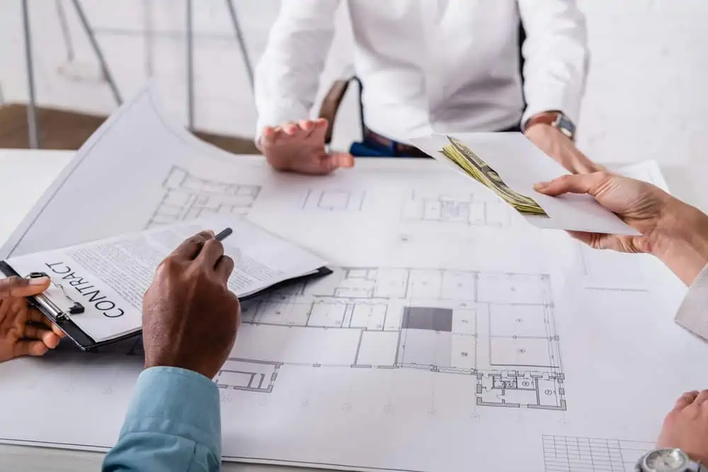 Business people looking over building floor plans, documents and exchanging money.