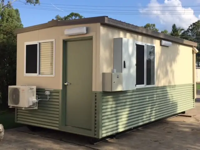 A small beige and green modular building with windows and air conditioning unit